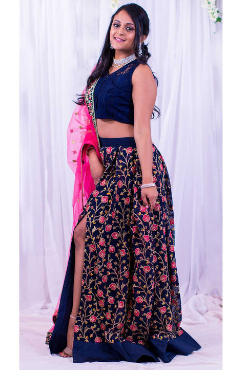 Two piece lehenga with high slit in blue skirt, covered in pink flower embroidery and gold stems. Paired with lacy blue blouse. Finish this look by draping hot pink dupatta with flower border on shoulders/ shoulder.