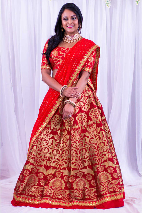 Beautiful two piece silk bridal lehenga. Skirt designed with traditional gold borders and flower design, paired with mid length sleeves blouse, covered in golden flowers. Finish this look by draping matching red dupatta covered in gold specks and flower border on shoulder.