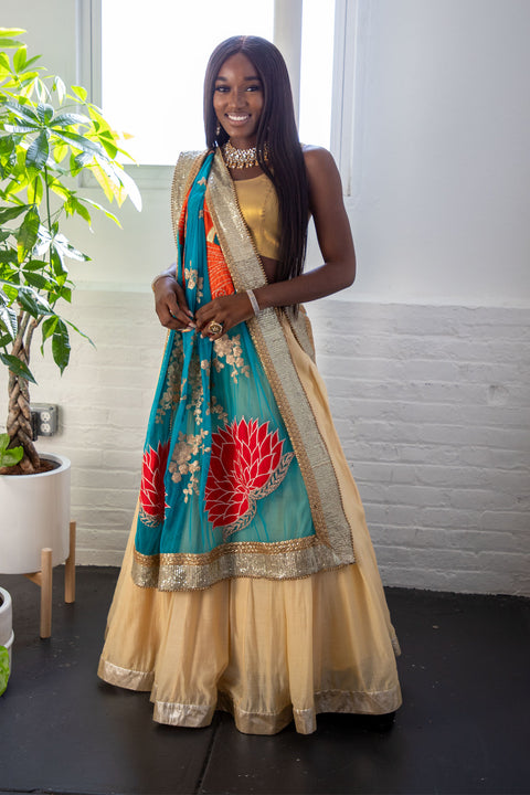 Let the colors fade to blue, why don't you.  Champagne lehenga paired with gold blouse. Finish this look with draping bright blue dupatta covered in red lotus flowers and heavy golden border on shoulders/ shoulder. Note: Blouse style may vary depending on size and availability  Skirt Length: 44 inches