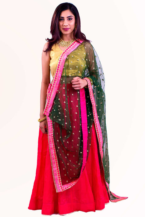 Fashionable two piece lehenga with crimson skirt decorated with dainty gold trim. Paired with gold blouse. Finish this look by draping a net green dupatta on shoulders/ shoulder.