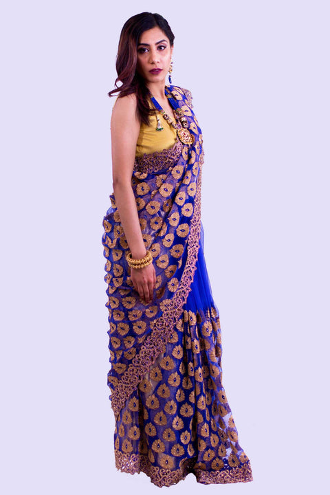 Royal blue net sari covered in iridescent gold embroidery. Pallu is decked in golden trim for high sophistication.