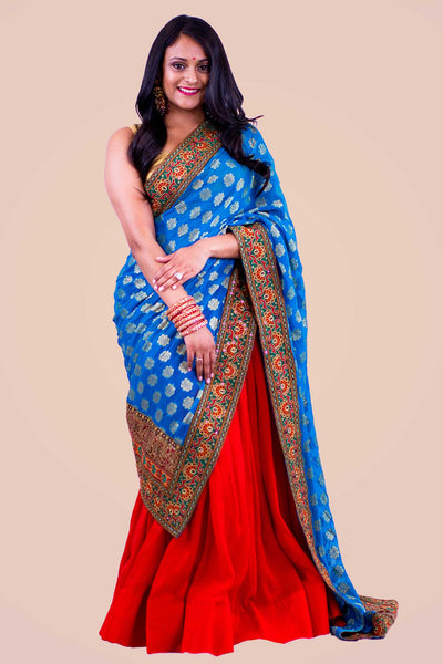 Phenomenal color blocking two piece lehenga, bright red skirt paired with golden blouse. Blue dupatta is focal point of this look, designed with heavy red and orange embroidered border.