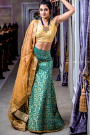 Sparkly two piece lehenga with green silk skirt covered in metallic design. Paired with radiant white silk blouse. Finish this look by draping the gold dupatta with flower trim and gold border on shoulders/ shoulder. 